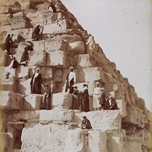 Close-up shot of the fallen down wall of the Pyramid of Cheops in Egypt. There are numerous Egyptians in traditional dress and European tourists climbing on the blocks of stone that make up the structure. Cairo, El Giza