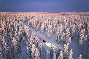 Aerial Views Fine Art Print Collection: Car traveling on icy road crossing the winter forest covered with snow from above, Lapland, Finland