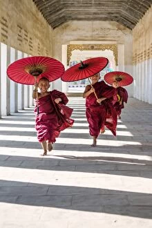 Boys Collection: Myanmar, Mandalay division, Bagan. Three novice monks running with red umbrellas in a walkway