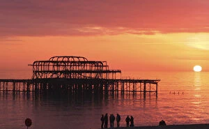 United Kingdom Metal Print Collection: Visitors watch the sun set behind the remains of the West Pier on the seafront at Brighton