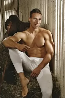 Temptation Collection: Man with a naked torso wearing long underwear in a horse barn sitting on bales of hay