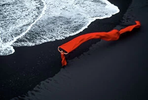 MIichael Melford Fine Art Print Collection: Lady in flowing red on a black sand beach at surf's edge in Iceland